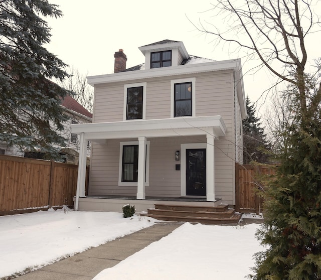 american foursquare style home with covered porch, a chimney, and fence