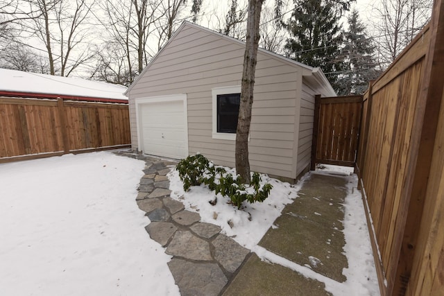 snow covered garage featuring a detached garage and fence