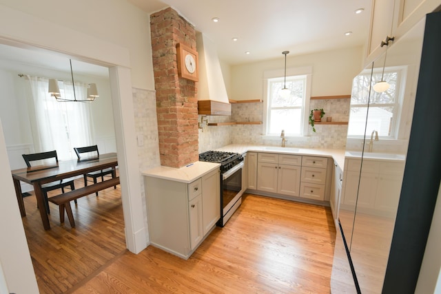 kitchen featuring open shelves, gas stove, a sink, light wood-type flooring, and wall chimney exhaust hood