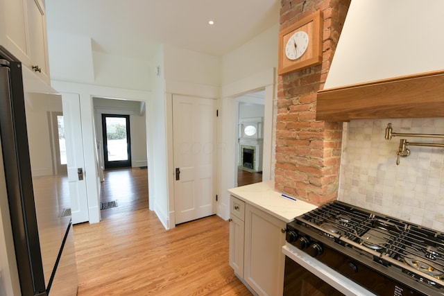 kitchen with visible vents, decorative backsplash, range with gas cooktop, light wood-style flooring, and light stone countertops