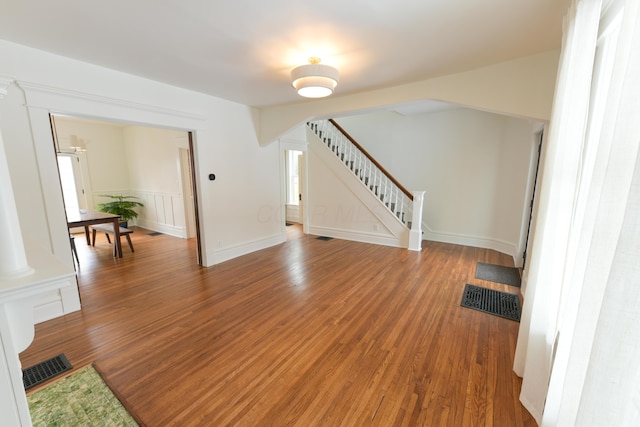 unfurnished living room featuring stairway, visible vents, arched walkways, and wood finished floors