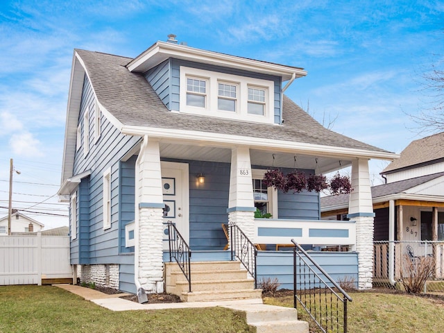 bungalow featuring covered porch, a front yard, fence, and roof with shingles