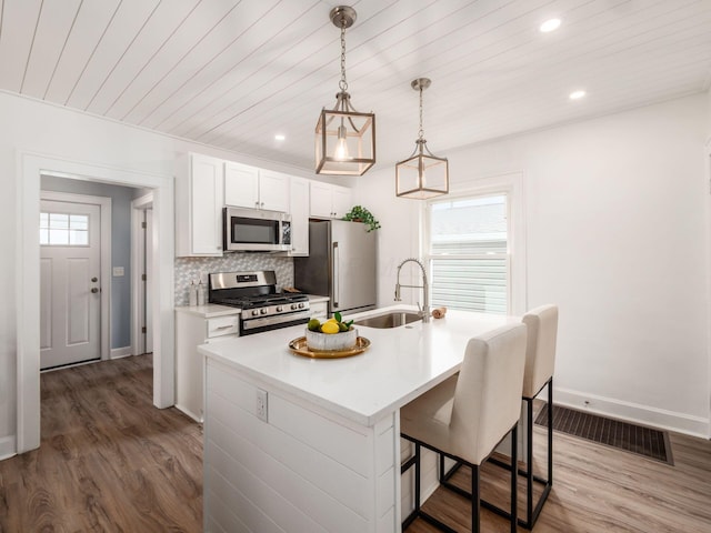 kitchen with wood finished floors, a sink, visible vents, appliances with stainless steel finishes, and backsplash