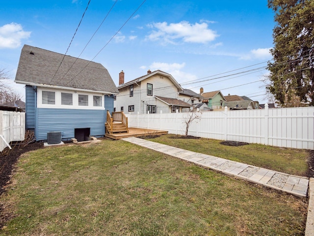 rear view of house featuring roof with shingles, a lawn, central AC, and fence