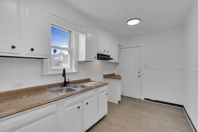 kitchen featuring white cabinets, a sink, light wood-type flooring, under cabinet range hood, and baseboards