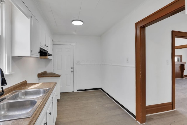 kitchen featuring light wood finished floors, white cabinetry, a sink, under cabinet range hood, and baseboards