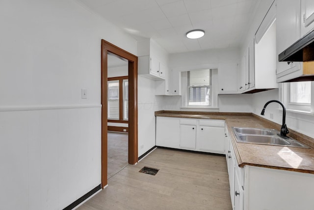 kitchen with visible vents, white cabinets, a wainscoted wall, light wood-style floors, and a sink