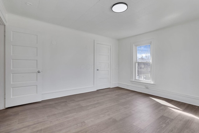 spare room featuring ornamental molding, baseboards, and wood finished floors