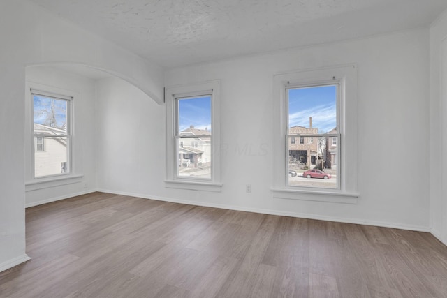 spare room featuring a textured ceiling, arched walkways, wood finished floors, and baseboards