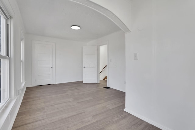 empty room featuring arched walkways, light wood-style flooring, and baseboards