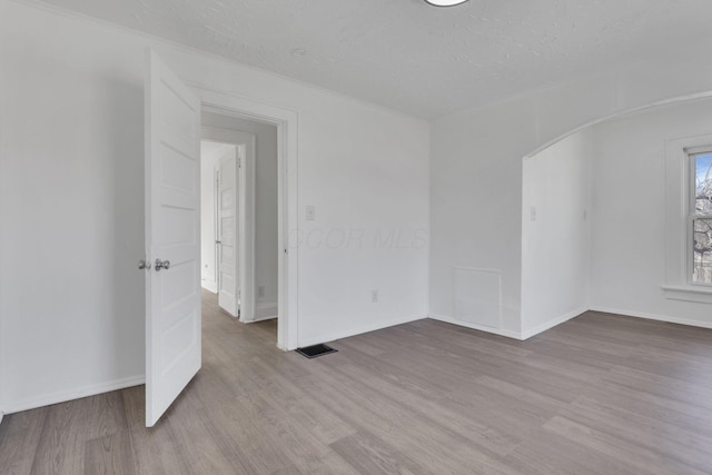 empty room featuring arched walkways, a textured ceiling, wood finished floors, visible vents, and baseboards