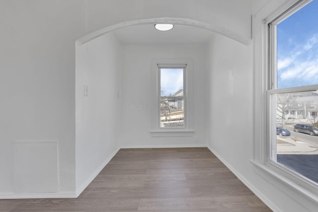 spare room featuring baseboards, arched walkways, and wood finished floors