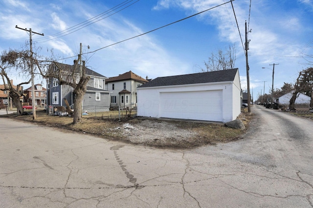 view of front of property featuring a garage, a residential view, fence, an outdoor structure, and stucco siding