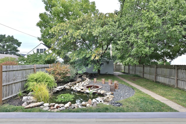 view of yard featuring an outdoor fire pit, a fenced backyard, and a garden pond