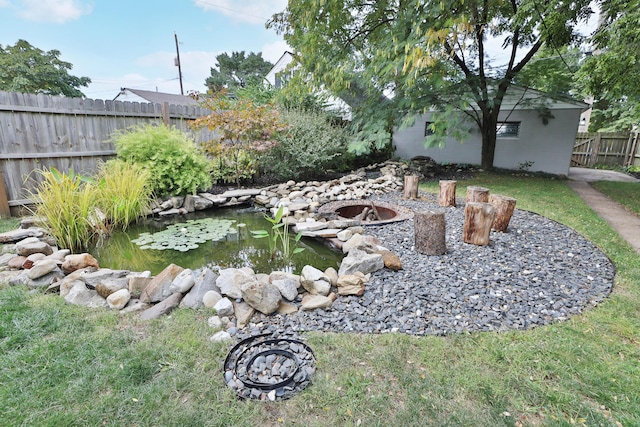 view of yard with a fire pit, fence, and a small pond