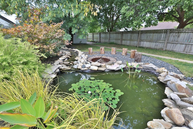 view of yard featuring a fire pit, a small pond, and fence