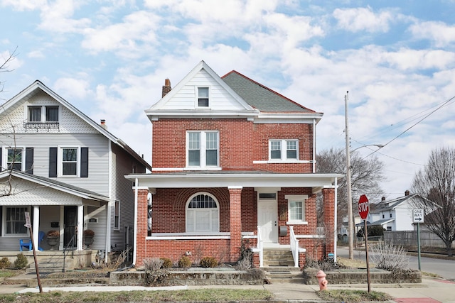 view of front of property with covered porch, a shingled roof, a chimney, and brick siding