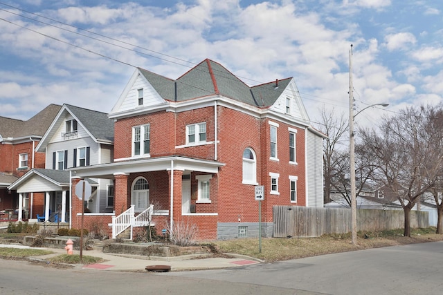 view of front of house featuring covered porch, fence, and brick siding