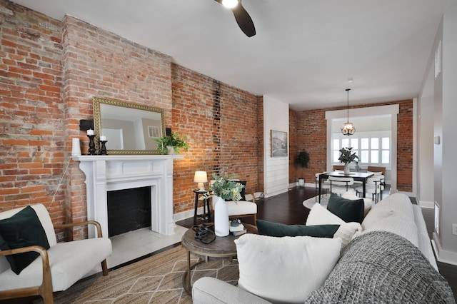 living area featuring a fireplace with flush hearth, a ceiling fan, brick wall, wood finished floors, and baseboards