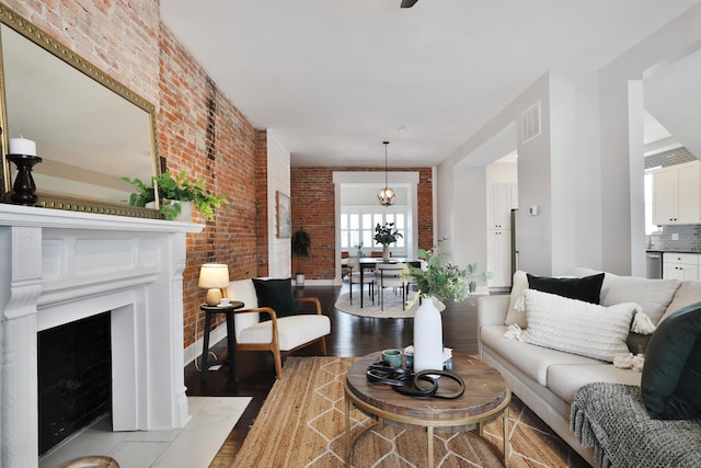 living area with a notable chandelier, brick wall, a fireplace, wood finished floors, and visible vents