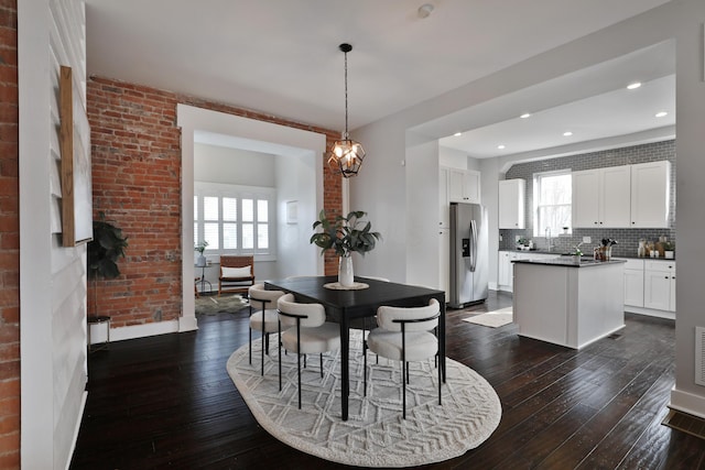 dining area with an inviting chandelier, brick wall, dark wood-style flooring, and recessed lighting