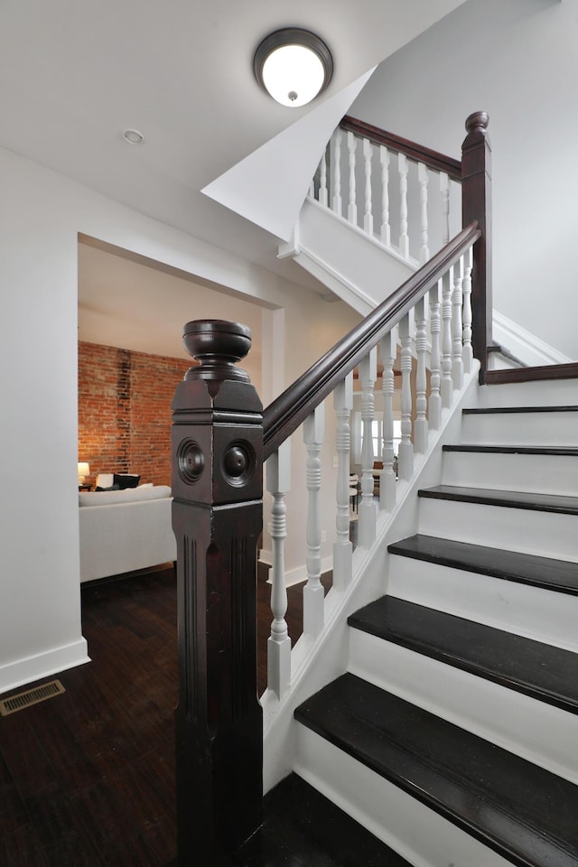 stairs with baseboards, brick wall, visible vents, and wood finished floors