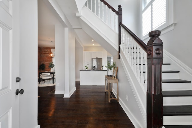 entrance foyer with baseboards, a towering ceiling, dark wood-style floors, stairs, and a notable chandelier