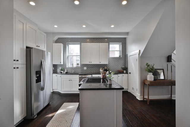 kitchen with stainless steel appliances, dark countertops, decorative backsplash, white cabinetry, and a sink