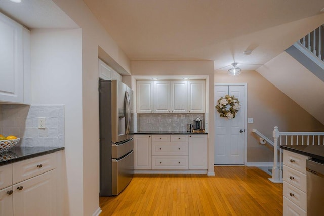 kitchen featuring baseboards, light wood finished floors, appliances with stainless steel finishes, white cabinetry, and tasteful backsplash