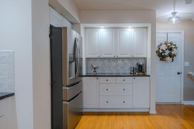 kitchen featuring light wood-type flooring, stainless steel refrigerator with ice dispenser, backsplash, white cabinetry, and baseboards