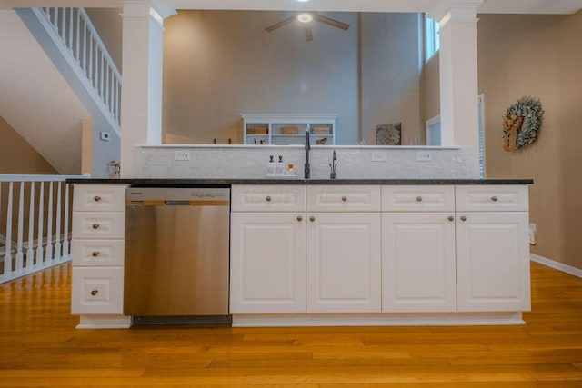 kitchen featuring dark stone counters, decorative columns, white cabinets, stainless steel dishwasher, and light wood-type flooring