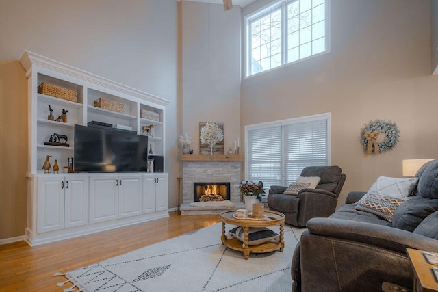 living room featuring light wood-type flooring, a high ceiling, and a stone fireplace