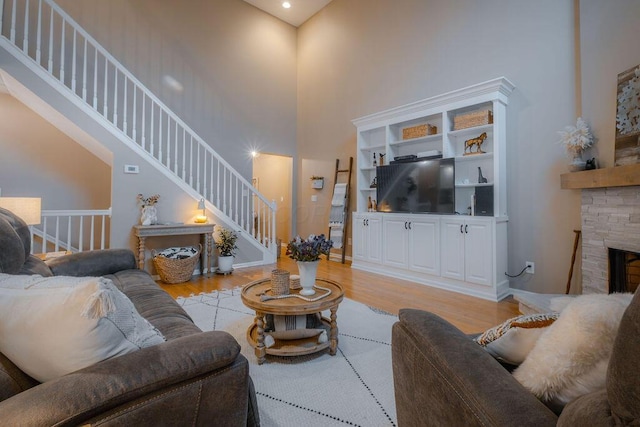 living room featuring a fireplace, stairs, light wood-style floors, and a towering ceiling