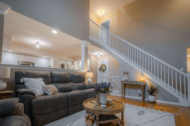 living area with stairway, wood finished floors, baseboards, a high ceiling, and decorative columns