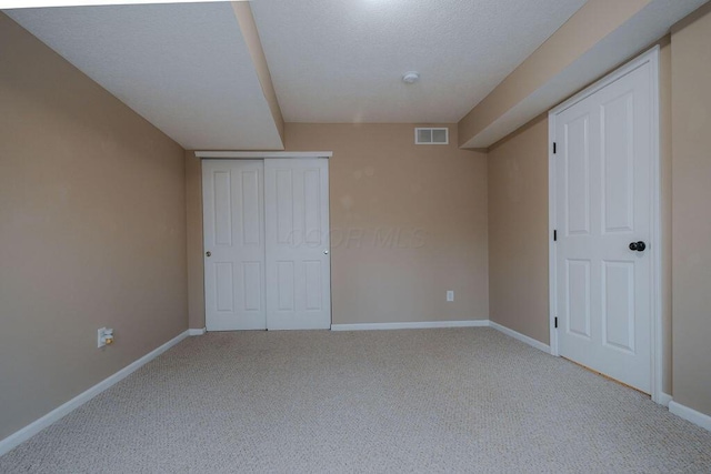 unfurnished bedroom with visible vents, baseboards, light colored carpet, a closet, and a textured ceiling