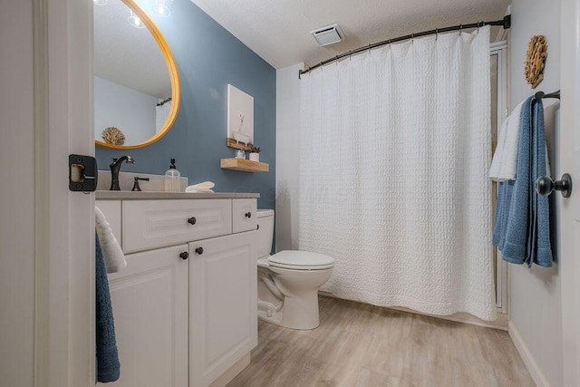 bathroom with visible vents, toilet, a textured ceiling, wood finished floors, and vanity