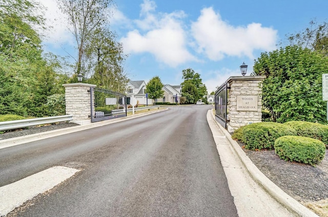 view of road with curbs, a gate, a gated entry, a residential view, and street lighting