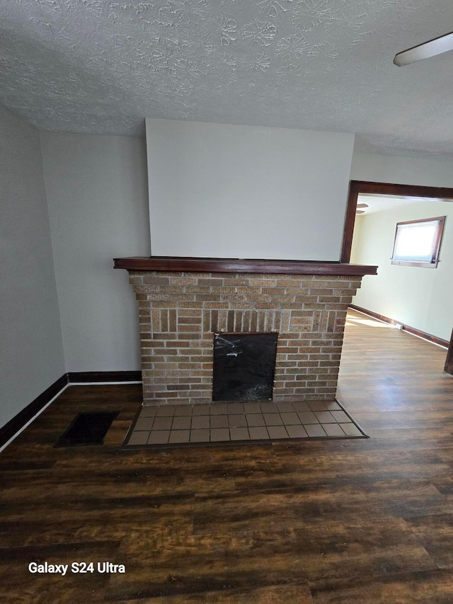 unfurnished living room featuring baseboards, a textured ceiling, wood finished floors, and a fireplace