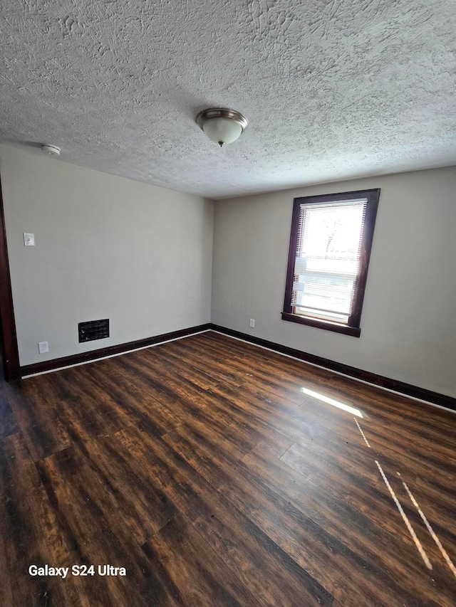 spare room featuring baseboards, dark wood-type flooring, and a textured ceiling