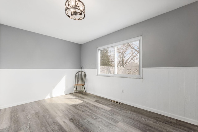 empty room with visible vents, a chandelier, wood finished floors, and wainscoting