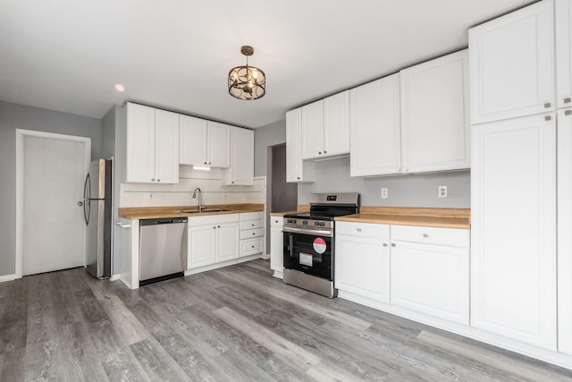 kitchen with stainless steel appliances, light wood-style flooring, white cabinets, a sink, and butcher block countertops