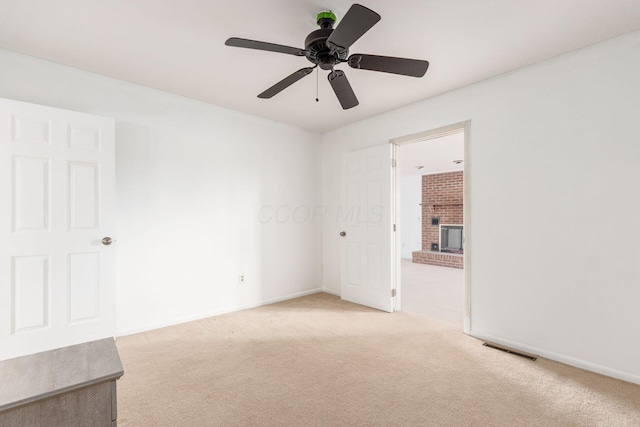 empty room featuring a brick fireplace, baseboards, visible vents, and light colored carpet