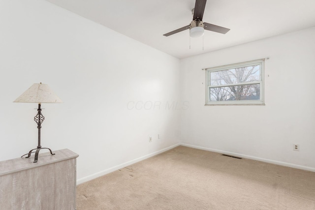 spare room featuring baseboards, a ceiling fan, visible vents, and light colored carpet