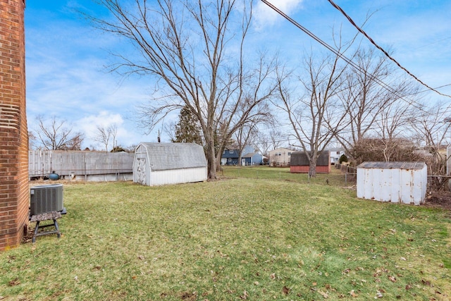 view of yard featuring central AC unit, a storage shed, fence, and an outbuilding