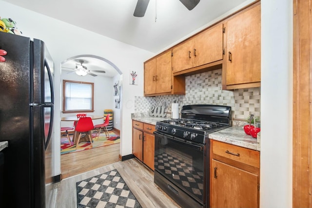 kitchen with arched walkways, light wood-style flooring, a ceiling fan, decorative backsplash, and black appliances