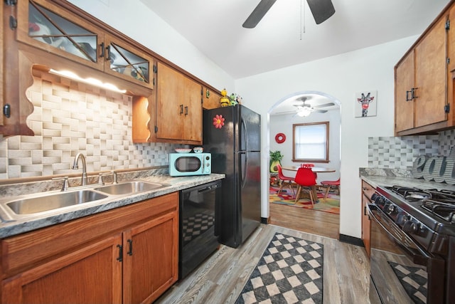 kitchen featuring arched walkways, tasteful backsplash, a sink, light wood-type flooring, and black appliances