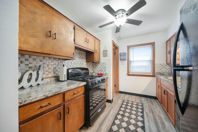 kitchen featuring baseboards, decorative backsplash, light wood-style flooring, brown cabinets, and black appliances