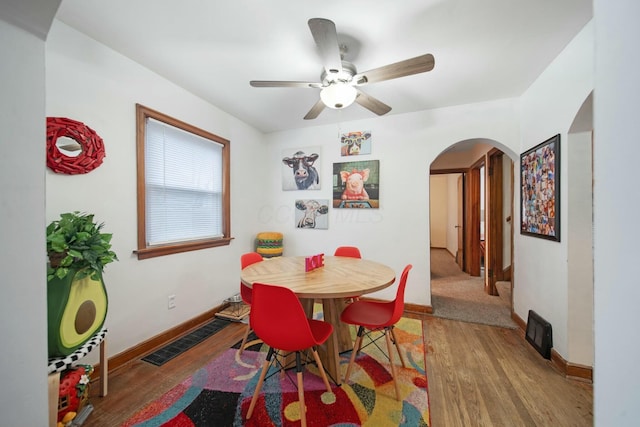 dining space featuring arched walkways, wood finished floors, visible vents, and baseboards