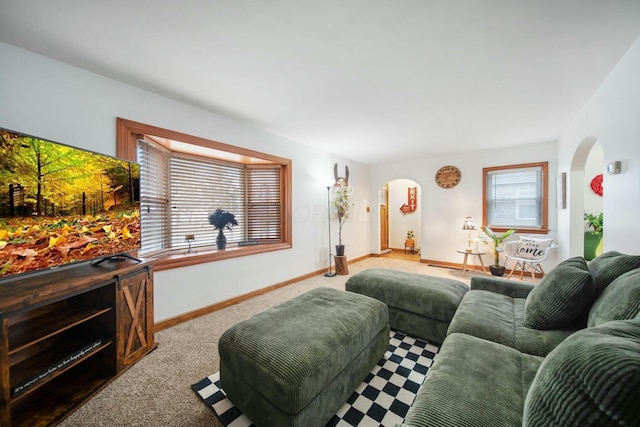 living area featuring carpet floors, baseboards, and arched walkways