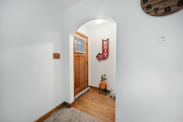 doorway with arched walkways, light wood-style flooring, and baseboards